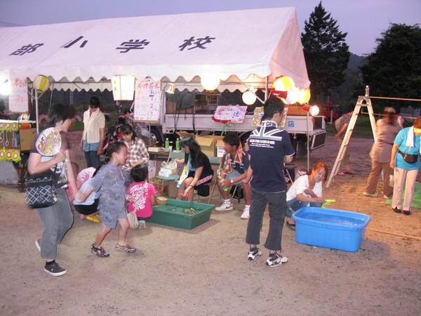 テントの外で大きなプラスチックの箱に水を張り、ボールを浮かべてる様子を子供達が見ている写真