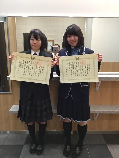 鏡の前で、女子高生2人がそれぞれ賞状を手に持ち記念撮影写真