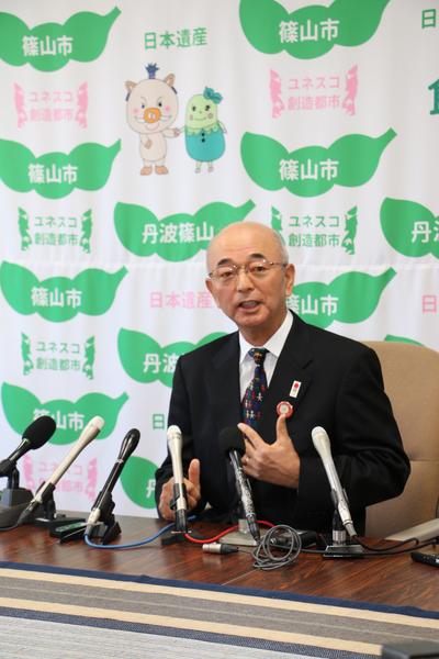 市長がたくさんのマイクの前でお話している写真