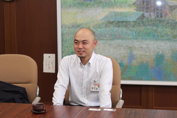 笑顔の西本 達也さんが椅子に座っており、一人で写っている写真