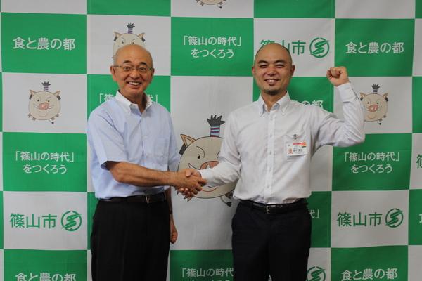 市長と西本 達也さんが握手しており、西本 達也さんが右手をガッツポーズしている様子の写真