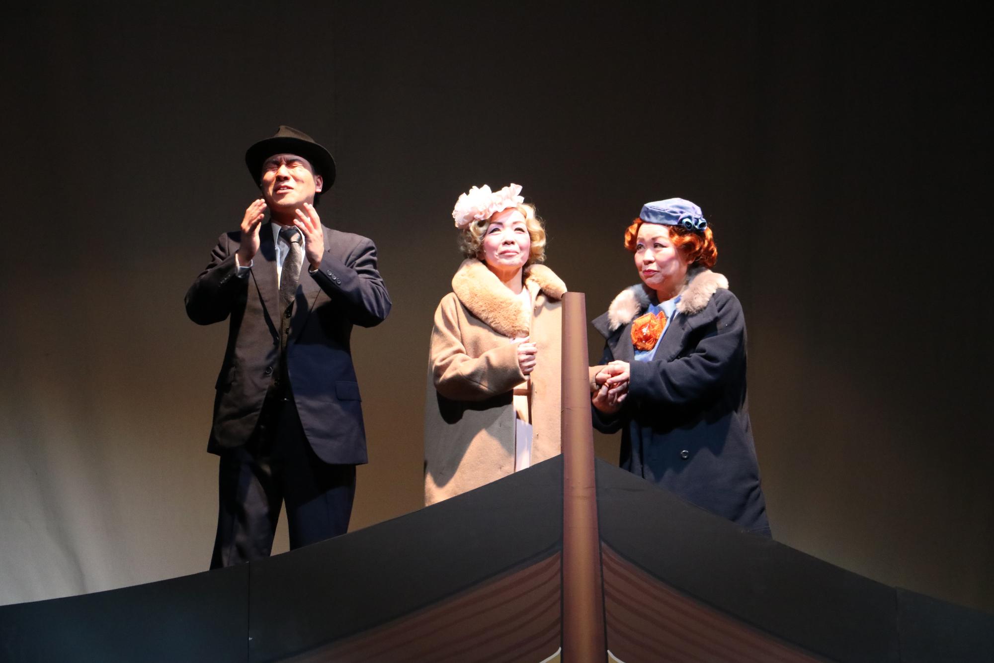 背広を着た男性の新聞記者と、ベージュのコートを着たヘレン・ケラーと、紺色のコートを着た秘書が船の先端に乗って、人生を振り返っている写真