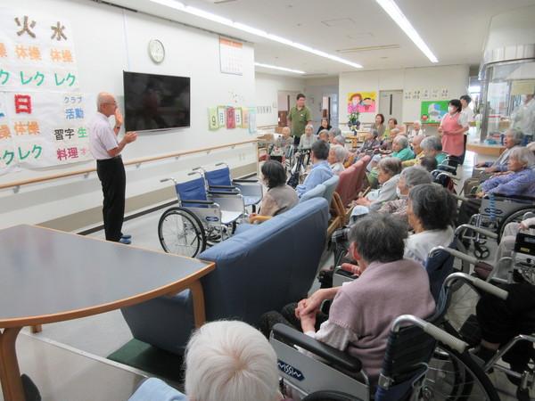 咲楽荘で市長が前で立って話をし、車いす、ソファーに座って聞いている高齢者の写真