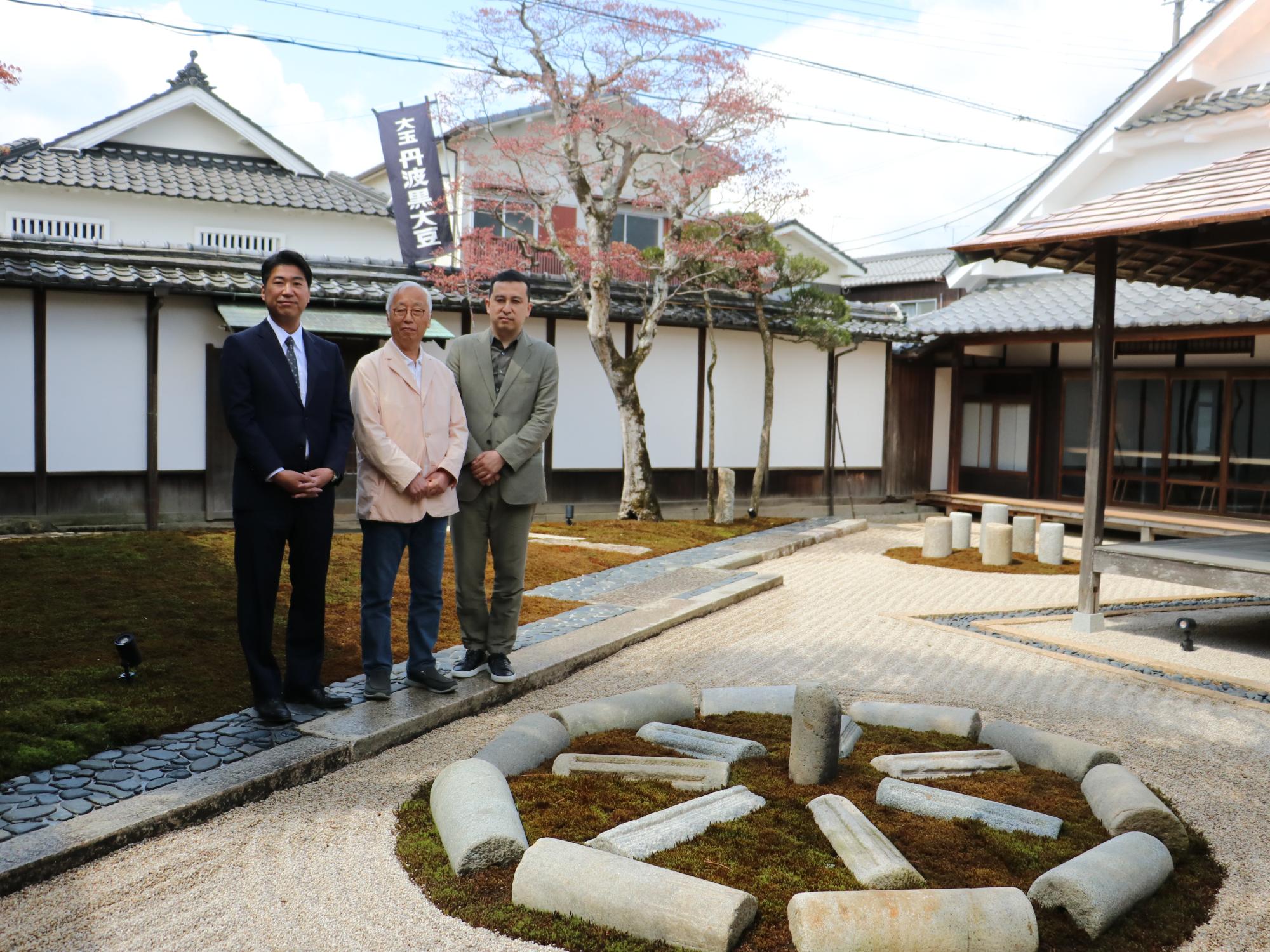 石庭の隣で男性3人が立っている。