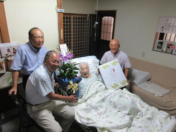 市長がお祝い品を持ち、ベッドのおばあちゃんと関係者で記念写真