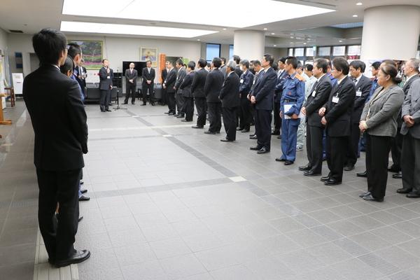 職員の方々が整列して並んでおり、マイクを持って話をしている男性の話を真剣に聞いている様子の写真