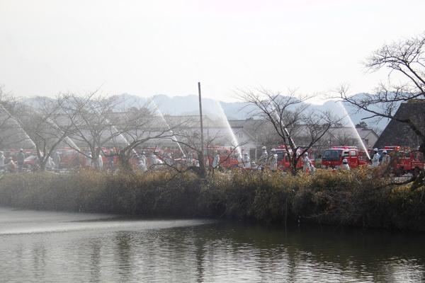 消防団員らが池に向かって放水演習を行っている写真