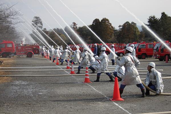 消防団員らが消防車のホースを持ち、放水演習を行っているのを左側から撮影されている写真