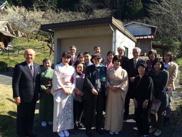 白い建物の前で杖を持った老人を中心に着物をきた女性やスーツをきた男性が並んでいる写真