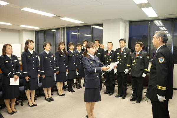制服を着た消防団の男女の前で、1名の消防団の女性が紙を見ながら読み上げている写真