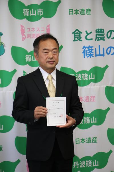 農都創造政策官に就任された森本 秀樹さんが任命書を持って写っている写真