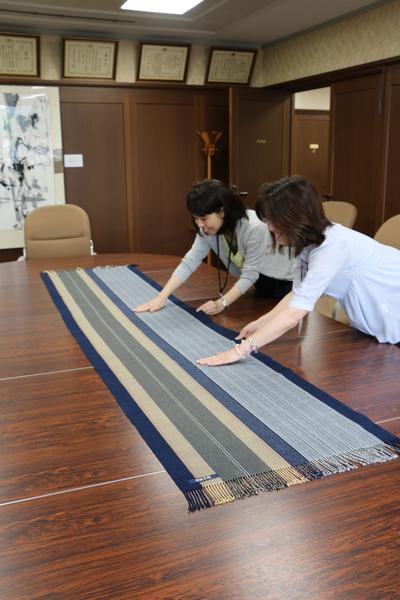 会議机に置かれたテーブルランナーを触っている女性2名の写真