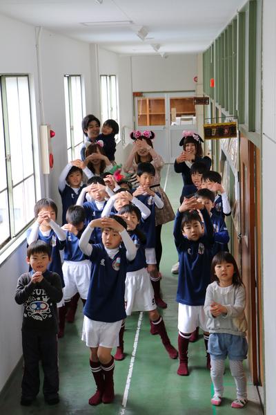 教室の廊下でユニフォームを着た男の子たちが、頭の上で手を使って丸を作っている写真