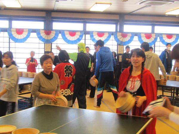 赤いマントをはおった女性と普段着姿の女性が桶で卓球をしている写真