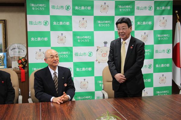 市長が座っていて、その横で佐藤町長が立って話をしている写真