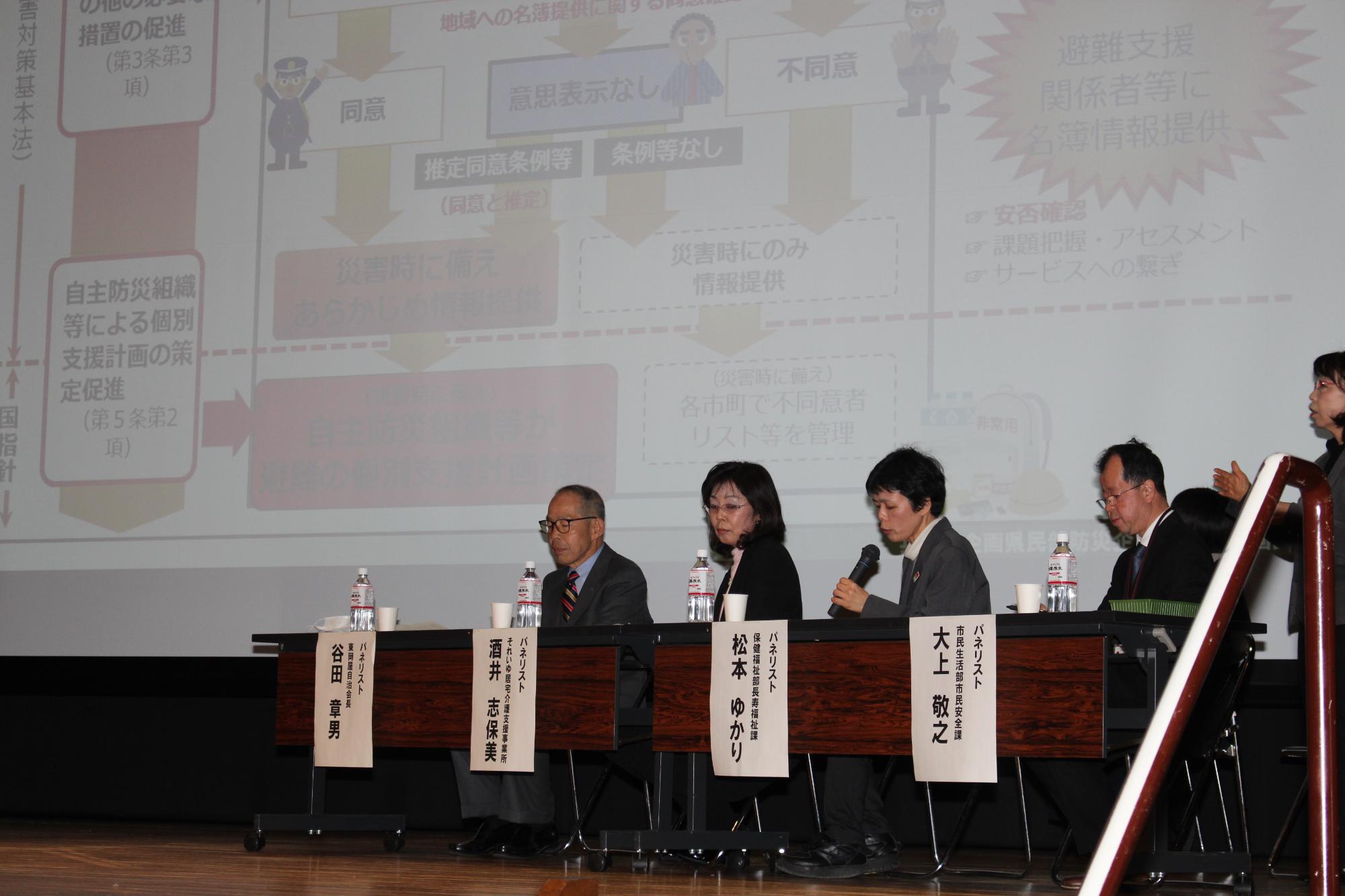 パネリストの松本ゆかりさんがマイクを持って話しているのを他の3人のパネリストが聞いている写真