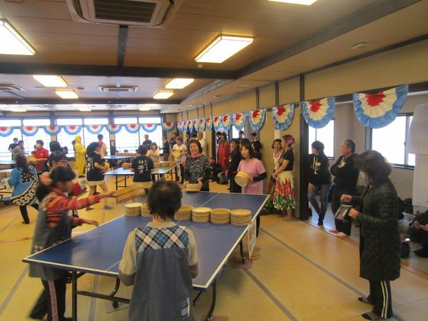 エプロンや割烹着を着た女性たちが桶で卓球をしている写真