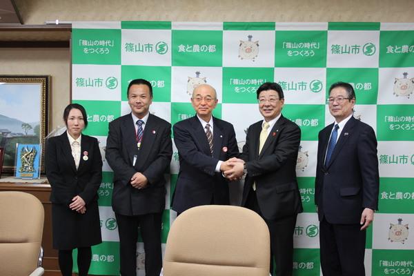 関係者3人の間で市長と佐藤町長が握手をして笑顔で記念撮影をしている写真