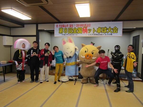 中央にまるいのの着ぐるみときつねの着ぐるみがいて、そのよこに7名男性が立っている集合写真