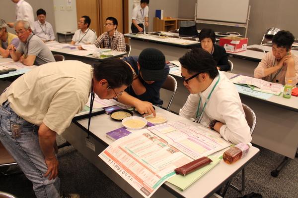 白い平たい皿にに入っている米を直接触って凝視している男性参加者3名の写真