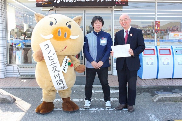 コンビニ交付と書いた紙を持ったまるいのと、水色の制服を着たコンビニの従業員の方と、酒井市長が横一列に並んでいる写真