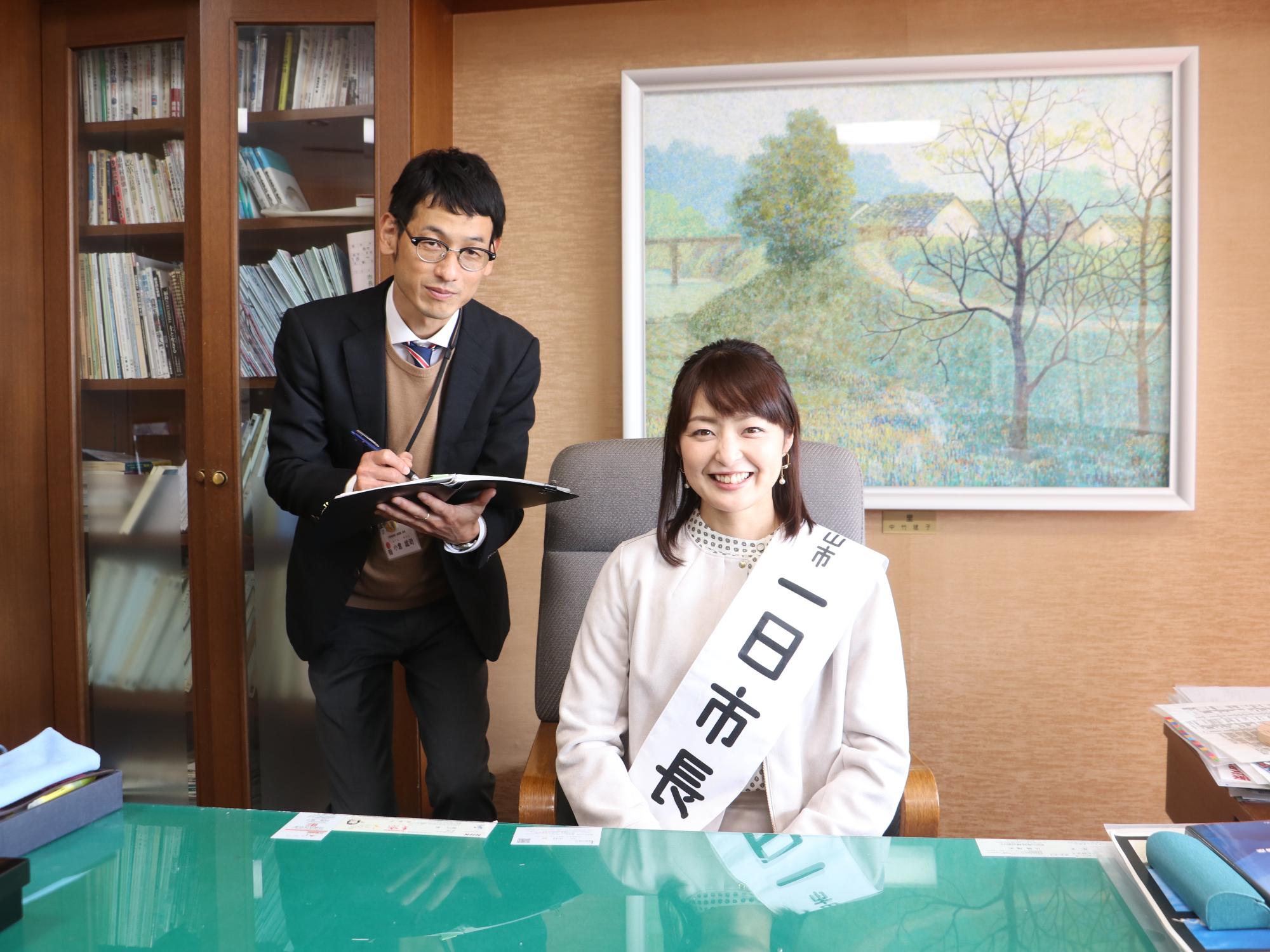 市長の椅子に座って秘書とスケジュールの確認をされている熊谷市長