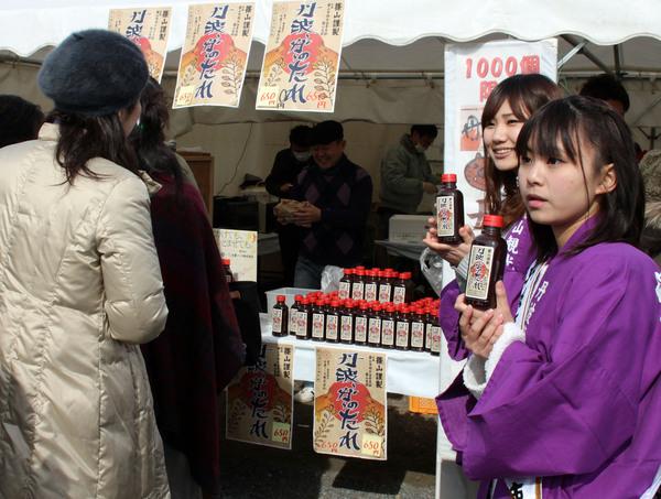 右側に法被を着た女性2人が丹波ーガーのたれを持って立っていて、中央にはたれがたくさん並べてあり販売されている写真