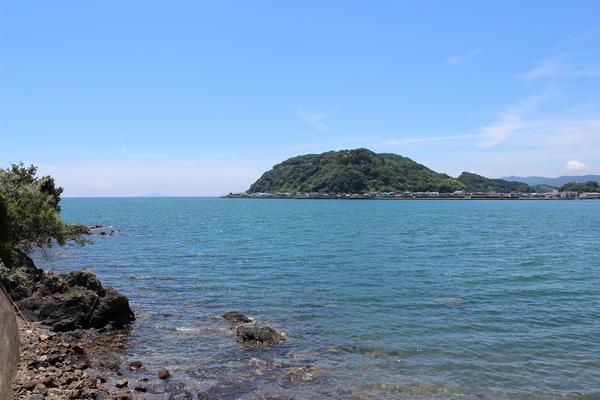 青空の下、透き通る海の奥に見える小さな島の写真