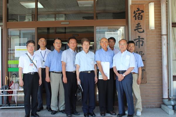 宿毛市役所とかかれた看板横の市役所入口で市長と関係者の人が並んで集合写真をとっている写真