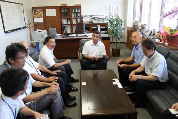 机を囲み座る、市長、清水町長、石川副町長と関係者の人が名刺交換をしている写真