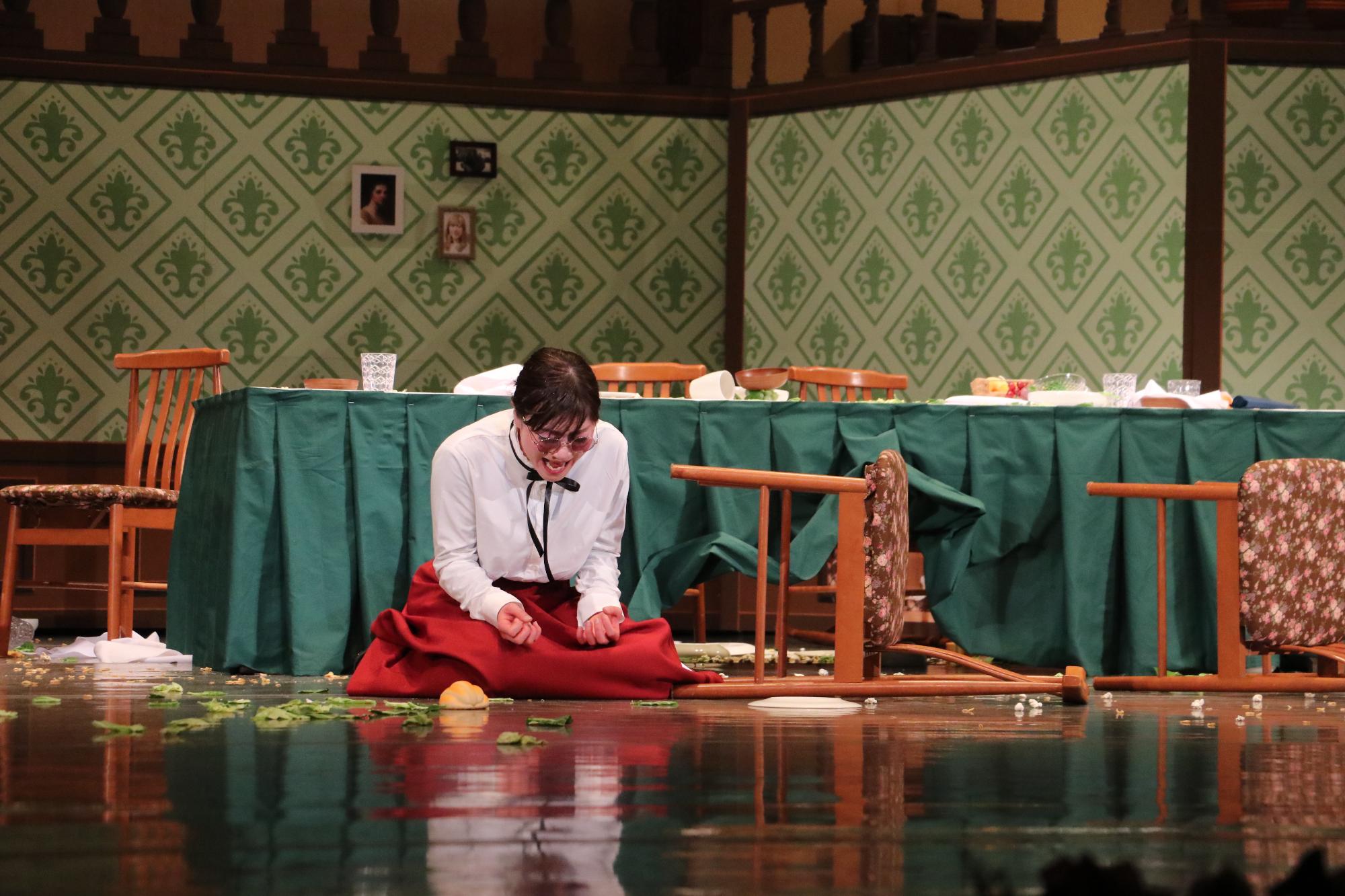 倒れたイスの横で座り込み、叫んでいるように見えるサリバン先生