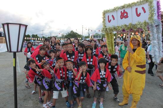 赤い法被にねじり鉢巻きをした子供達の横に「いぬい」とかかれたプラカードを持ったピカチュウの着ぐるみ姿の男性との集合写真