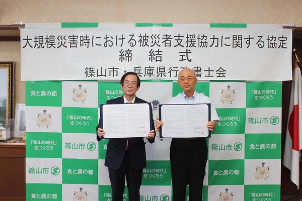 大規模災害時における被災者支援協力に関する協定締結式にて村山会長と市長が申請書類を持ち並んでいる写真