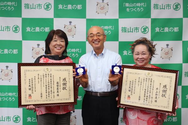 額に入った感謝状を持つ井上 和美さんと西田 直美さんの間にメダルを持つ市長が笑顔で写っている写真