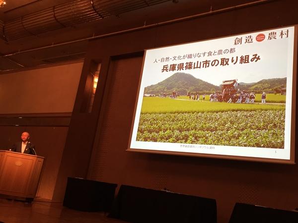 篠山市長が、兵庫県篠山市の取り組みと言うスライドの左側で、話をしている写真