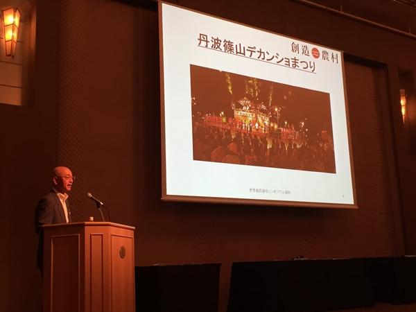 篠山市長が、丹波篠山デカンショまつりのスライドの左側で話をしている写真
