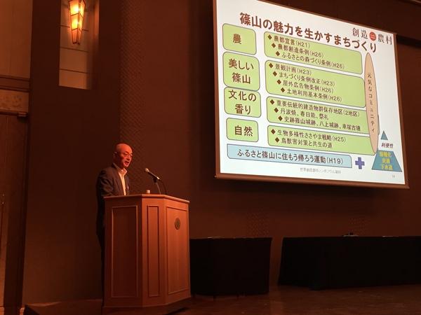 篠山市長が、篠山の魅力を生かすまちづくりについてのスライドの左側で話をしている写真