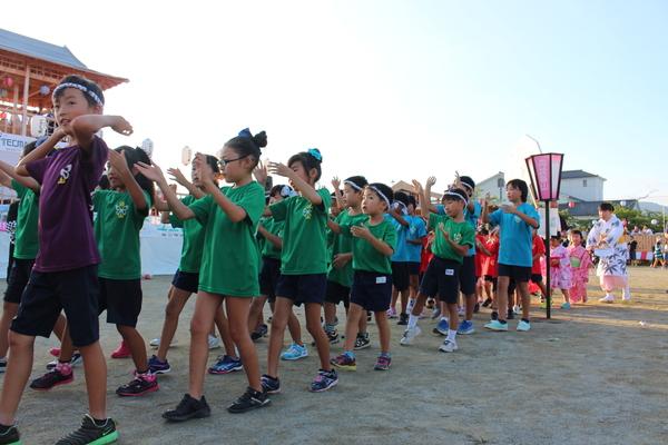 緑のTシャツ、水色のTシャツにねじり鉢巻きの子供達が列になり踊っている写真