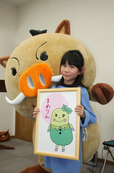 まめりんの公式デザインを手に持っている道本 彩葉（みちもと あやは）さんの後ろにキャラクターまるいのが顔を出している写真