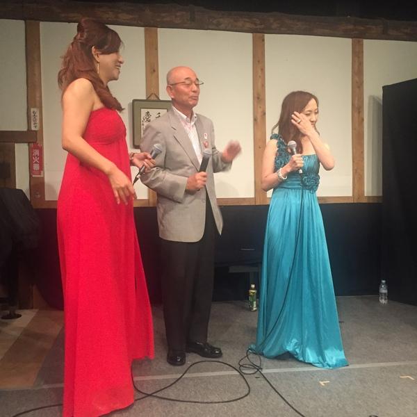 市長が水色と赤の衣装をきたアカペラグループの女性2人と一緒にステージに立っている写真