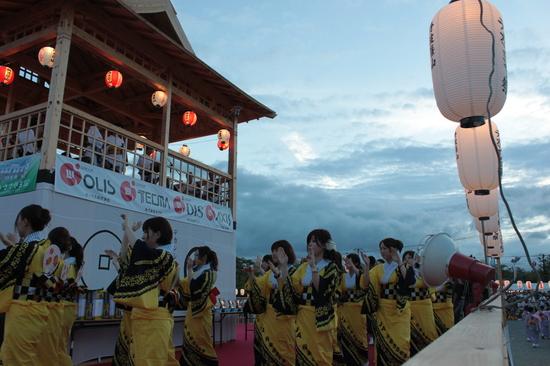 薄暗い舞台の下で黄色い浴衣を着た女性たちが踊っている写真