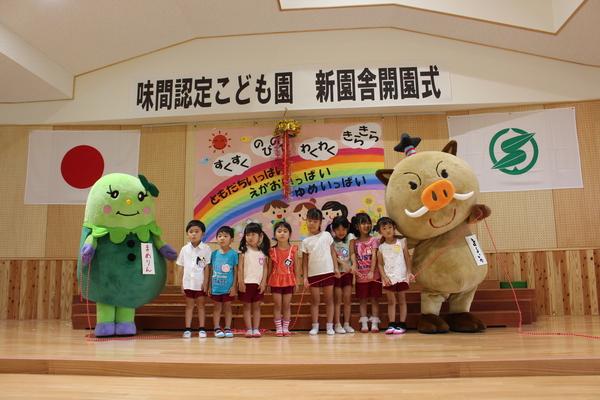 味間認定子ども園 新園舎開園式とかかれた幕の前で8名の子供たちと、篠山市のキャラクターまるいの、まめりんが並んでいる写真