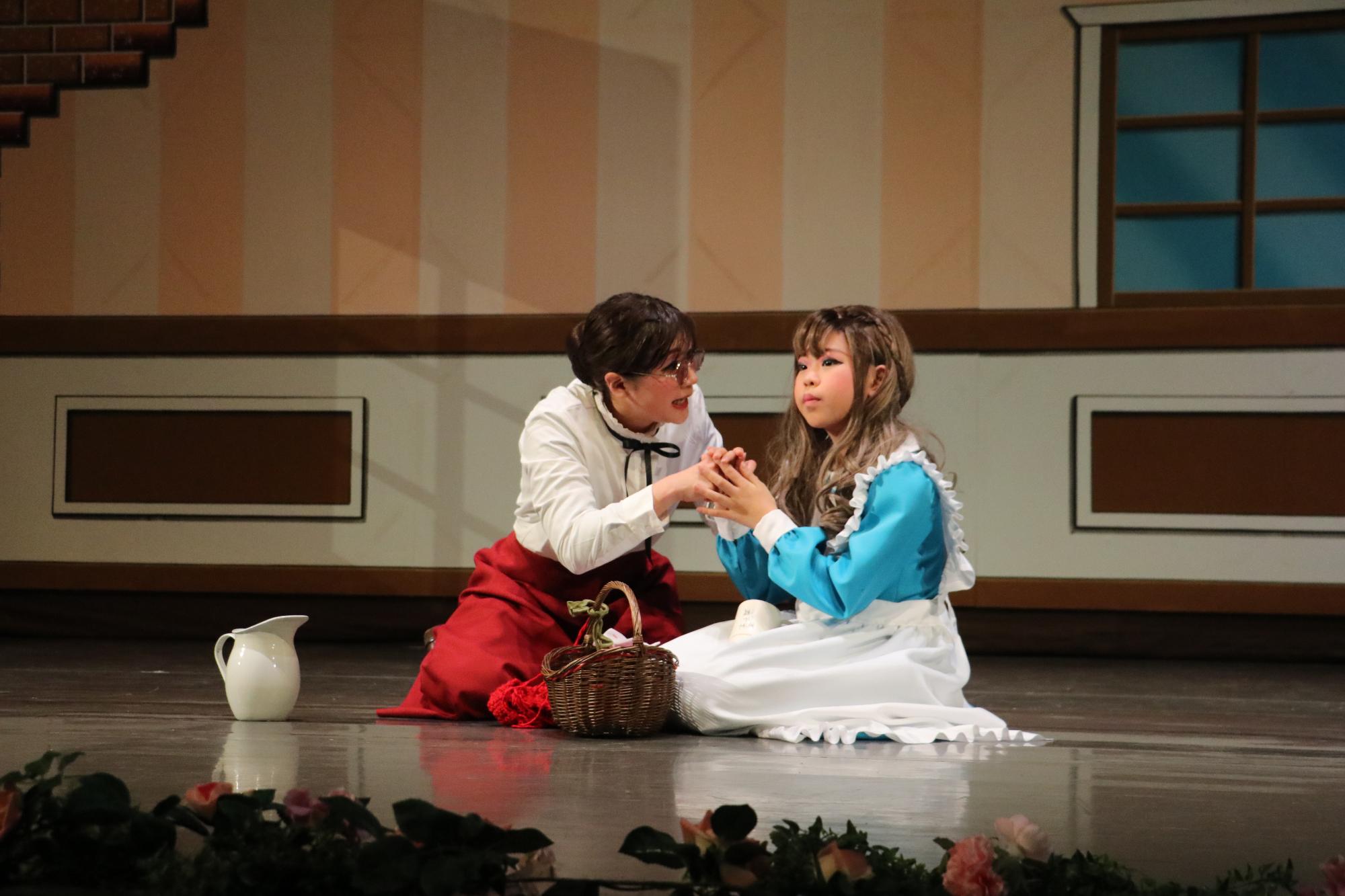 指文字を教えるために地面に座っているヘレンとサリバン先生がお互いの手を握り、サリバン先生がヘレンに対して一生懸命伝えている写真