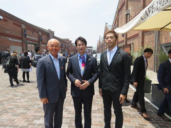 展示場の建物の前で並ぶ、スーツを着た3人の男性の写真