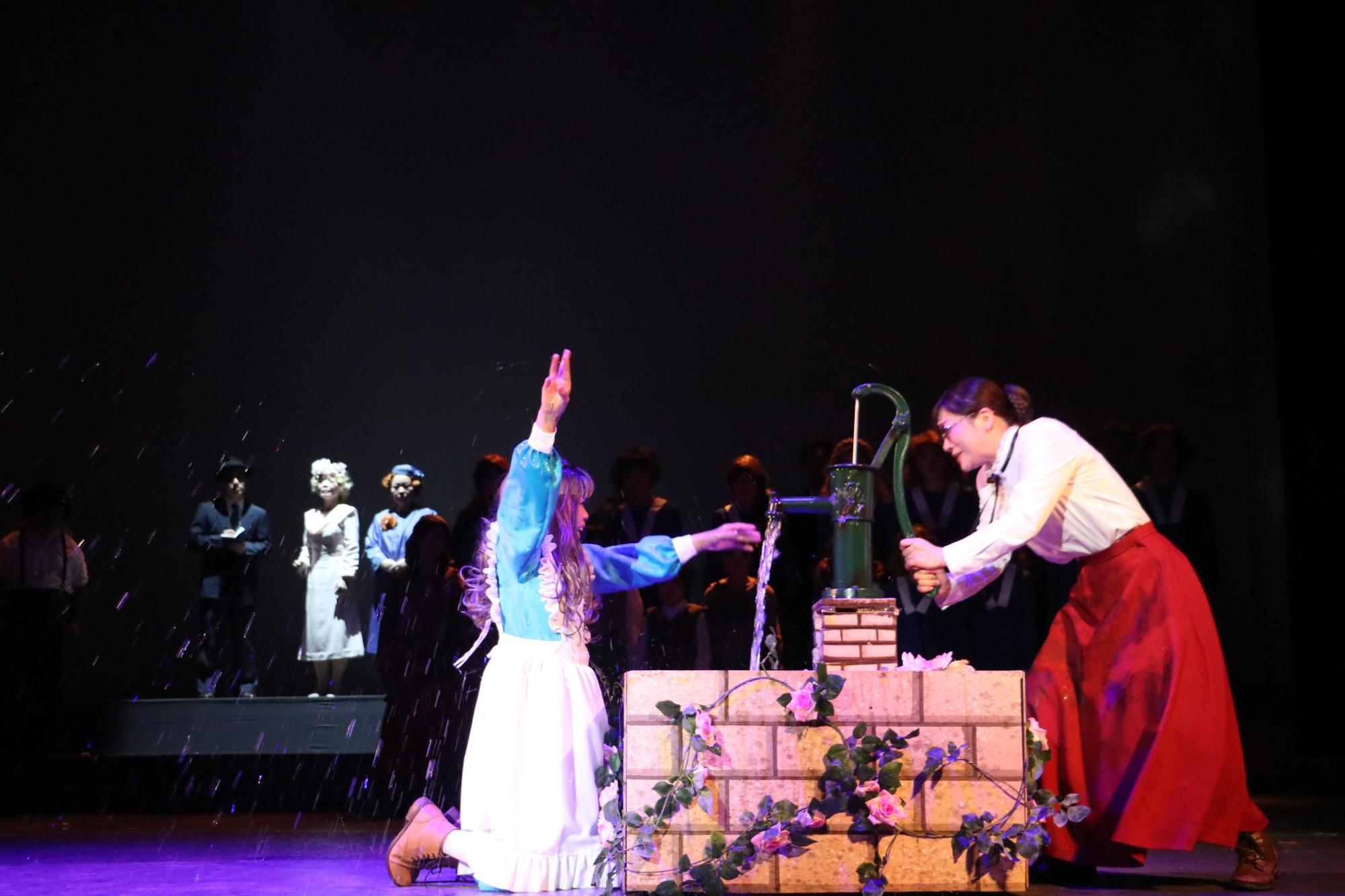 井戸のようなところでサリバン先生が水を引き、ヘレンが右手をあげ左手でそこから出ている水に触れようとしている写真