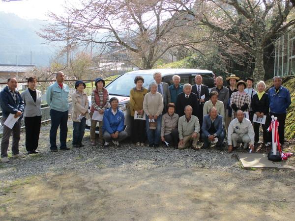 グレーの自家用車の前に、出発式の参加者が集まって写っている記念写真