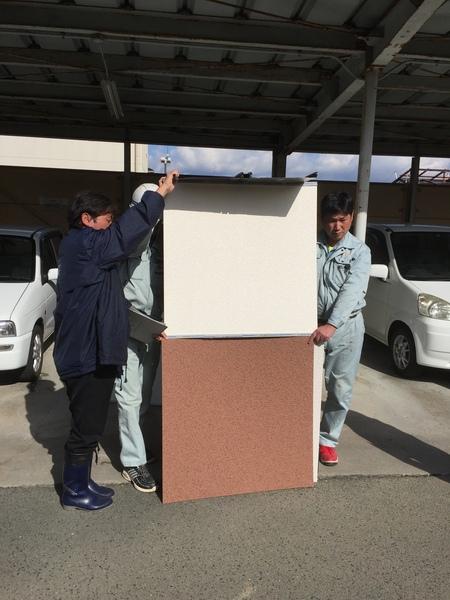 作業員服の男性3名が1メートルほどの正方形の壁の見本を縦に2枚持っている写真