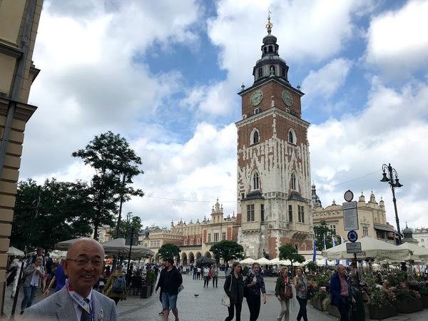 市長の後ろに茶色と白で出来た高い建物が建っている写真