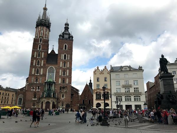 右側に白い建物、左側に茶色の高い建物が建っていて、前の広場に沢山の人達が歩いている写真
