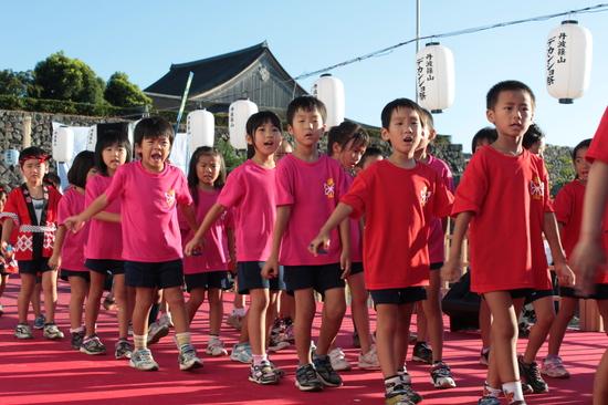 赤いカーペットの上を赤やピンクのティシャッを着た子供達が歩いている写真